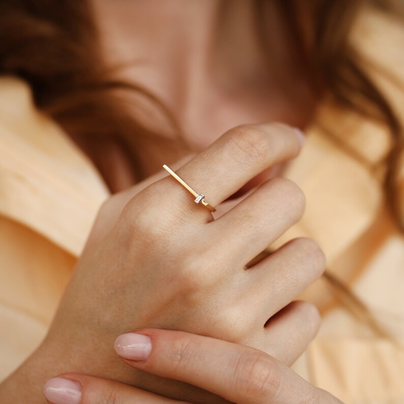 May include: A gold ring with a thin, straight band and a small, clear diamond set in the center.