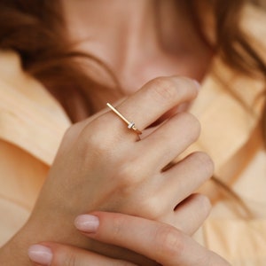 May include: A gold ring with a single, small, clear diamond set in a thin, straight band.
