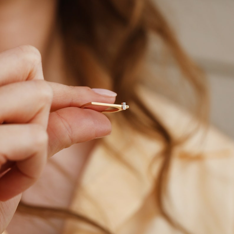 May include: A thin gold band ring with a single small diamond set in the center.