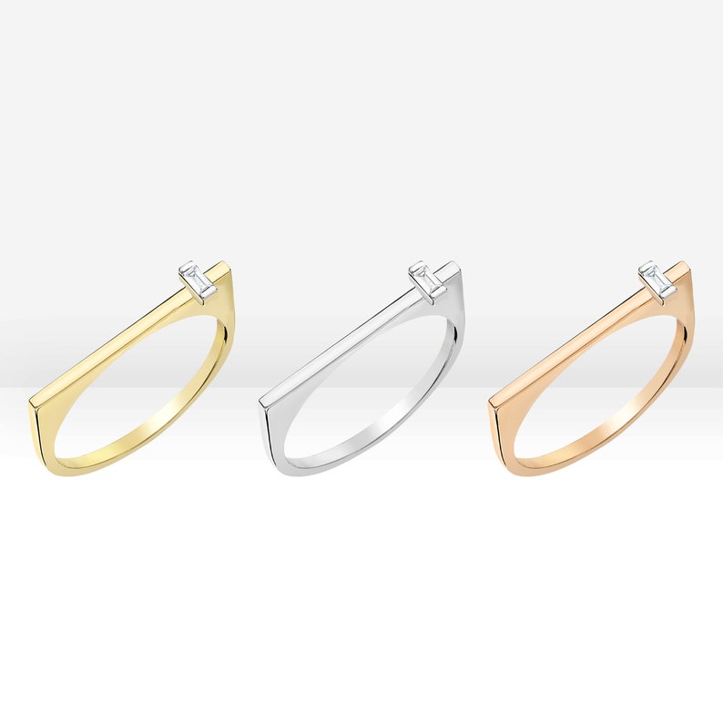 May include: Three minimalist rings with a single diamond set in a rectangular band. The rings are available in gold, silver, and rose gold.