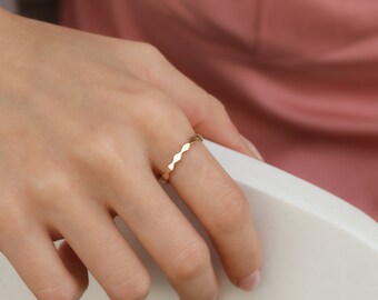 May include: A thin gold ring with a wavy, textured band.