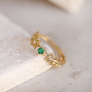 May include: A gold ring with a delicate leaf design and a single green gemstone. The ring is set with small white gemstones.