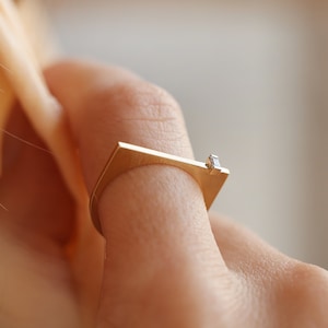 May include: A gold ring with a square band and a small diamond set in the top.