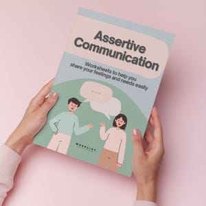 Op de afbeelding: Een paperback boek getiteld "Assertive Communication" met illustraties van twee mensen die in gesprek zijn. De omslag is lichtblauw en groen met de tekst "Worksheets to help you share your feelings and needs easily."