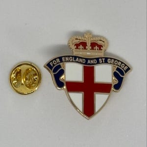 May include: A gold-toned metal lapel pin featuring a shield with a red cross on a white background, topped with a crown. A blue banner across the top reads FOR ENGLAND AND ST GEORGE in gold lettering. A separate gold-toned metal pin back is included.