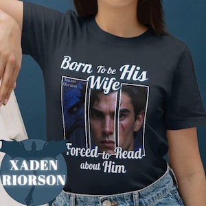 Peut inclure: Un t-shirt bleu marine avec le texte "Born To be His Wife" et "Forced-to-Read about Him". Le t-shirt présente également une photo d'un homme avec un dragon.