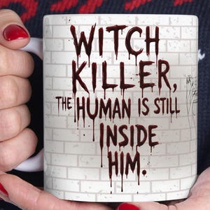 Pu&ograve; includere: Tazza in ceramica bianca con la scritta "WITCH KILLER, THE HUMAN IS STILL INSIDE HIM." in rosso scuro gocciolante. Lo sfondo presenta un disegno a muro di mattoni bianchi. La tazza &egrave; tenuta da una persona con lo smalto rosso.