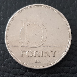 May include: A silver Hungarian Forint coin with the letter "D" and the word "FORINT" inscribed on it.