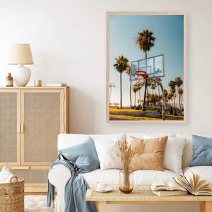 May include: A framed print showing a basketball hoop with a red net, set against palm trees and a blue sky. The word "Clippers" is on the backboard. The image has a sunny, coastal feel, reminiscent of a beachside location.