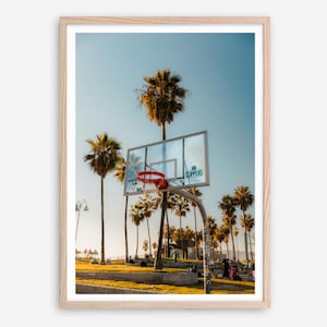 May include: A framed photograph featuring a basketball hoop with a red net, set against a backdrop of palm trees and a clear blue sky. The word "Clippers" is visible on the backboard.