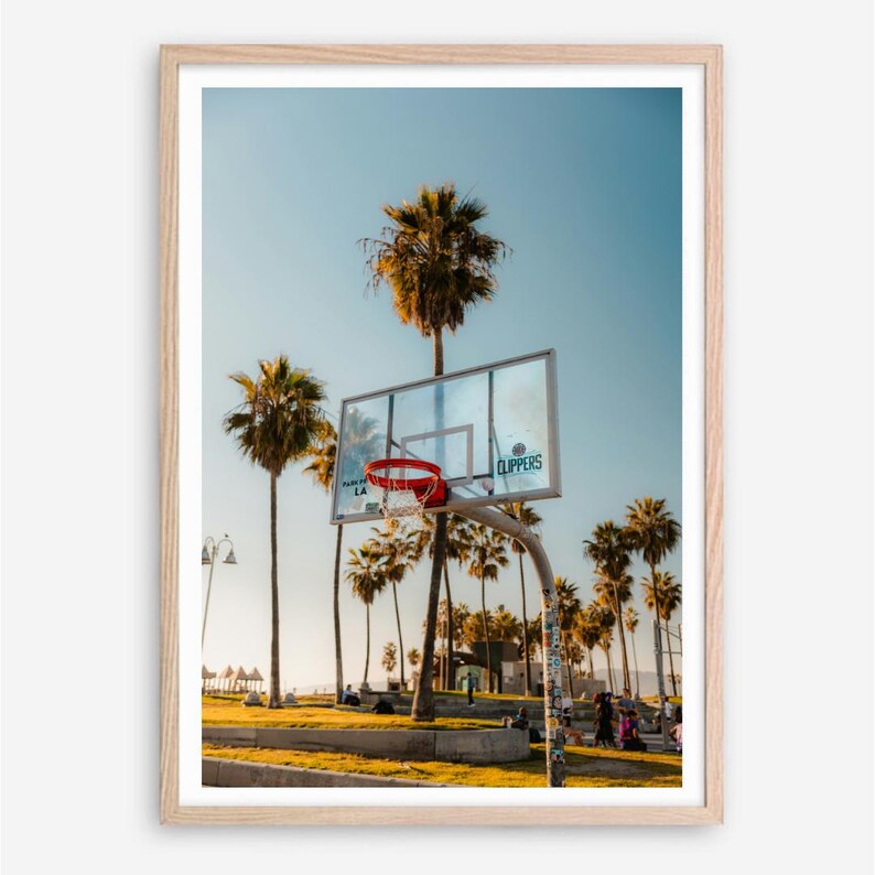 May include: A framed photograph featuring a basketball hoop with a red net, set against a backdrop of palm trees and a clear blue sky. The word "Clippers" is visible on the backboard.