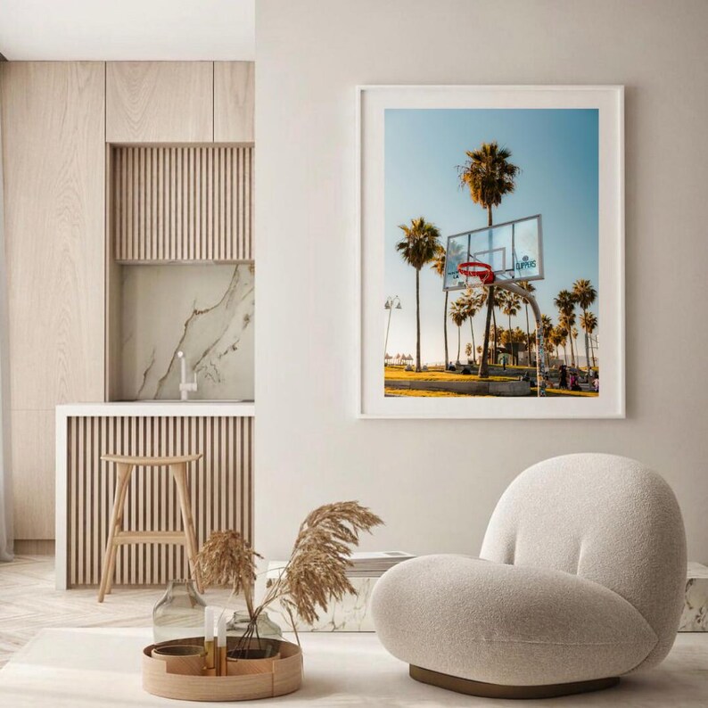May include: A framed print featuring a basketball hoop with a red net, set against a backdrop of palm trees and a clear blue sky. The print is displayed in a white frame, suitable for home decor.