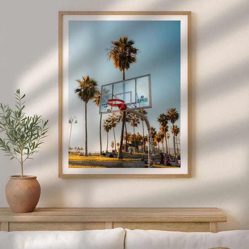 May include: A framed print showing a basketball hoop with a red net, set against palm trees and a blue sky. The word "Clippers" is visible on the backboard. The scene evokes a sunny, outdoor sports theme.