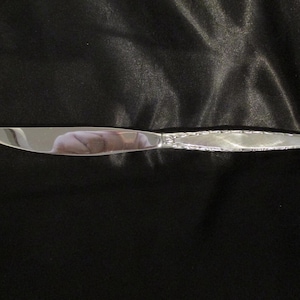 May include: A silver butter knife with a decorative pattern on the handle.