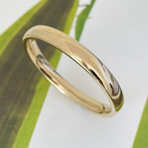 Könnte beinhalten: Ein schlichtes goldenes Armreif-Armband mit glatter, polierter Oberfläche.