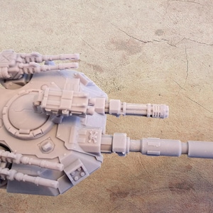 May include: A light grey miniature war machine with multiple gun turrets and a central cannon. The model has a detailed design with various mechanical components and antenna-like structures. The overall aesthetic suggests a science fiction or fantasy theme.