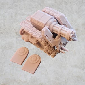 Puede incluir: Un modelo de tanque de plástico beige con un cañón grande de varios cañones. El tanque tiene orugas y un diseño detallado. Se incluyen dos discos de plástico beige.