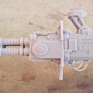 May include: A light gray, detailed miniature weapon, possibly a futuristic firearm or sci-fi prop. The design includes multiple barrels, a handle, and various mechanical components. The object is set against a neutral background.