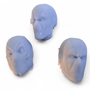 Könnte beinhalten: Drei graue, 3D-gedruckte Plastikköpfe eines maskierten Superhelden. Die Köpfe sind alle nach vorne gerichtet und haben ein ähnliches Design, aber mit leichten Variationen in den Details der Maske.