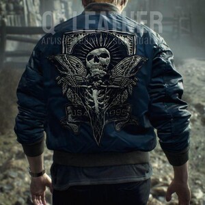 May include: A dark blue bomber jacket featuring a large back graphic of a skull with moth wings, a sunburst design, and a banner with the text U.S.A. 1995. The jacket has ribbed cuffs and a hem, worn over a dark shirt and black pants.