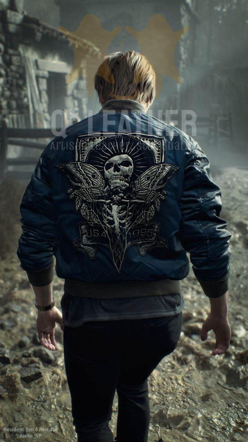 May include: A dark blue bomber jacket featuring a large back graphic of a skull with moth wings, a sunburst design, and a banner with the text U.S.A. 1995. The jacket has ribbed cuffs and a hem, worn over a dark shirt and black pants.