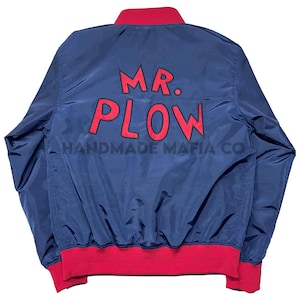 May include: A navy blue bomber jacket with a red ribbed collar and cuffs. The jacket has "MR. PLOW HANDMADE MAFIA CO." embroidered on the back in red.