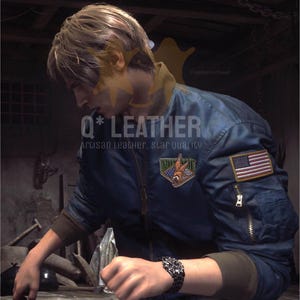 May include: A dark blue bomber jacket featuring a front zipper, brown ribbed cuffs, and a zippered utility pocket on the left sleeve. An American flag patch is on the sleeve, and a triangular patch with a graphic design is on the chest.