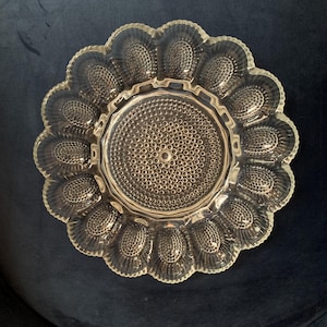 May include: Clear glass serving dish with a scalloped edge and a central circular design. The dish features a textured surface with a pattern of small, raised dots. The overall shape is reminiscent of a flower, suitable for serving appetizers or desserts.