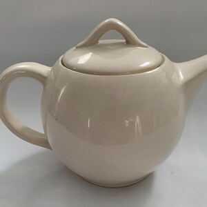 May include: A white ceramic teapot with a round body and a lid with a handle. The teapot has a spout on one side and a handle on the other.