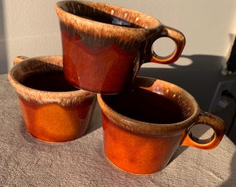 May include: Three brown and white glazed ceramic mugs with a drip glaze design. The mugs have rounded handles.