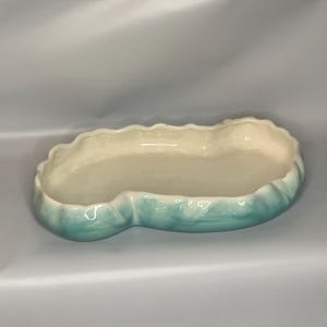 May include: A light blue ceramic dish with a scalloped edge. The dish is shaped like a leaf and has a white interior.