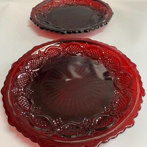 May include: Two red glass plates with a scalloped edge and a raised design. The plates are made of ruby red glass and have a vintage look.
