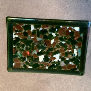 May include: Rectangular glass dish with a dark green border. The interior is a mosaic of green, brown, white, and orange glass pieces. The dish is likely handmade and suitable for decorative or functional use.