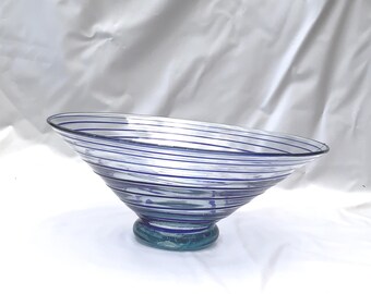 May include: A clear glass bowl with a wide, flared rim and a rounded base. The bowl is decorated with horizontal blue stripes. The base is a darker shade of blue and has a circular shape. The bowl is likely used for serving or display.