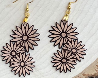 May include: A pair of dangle earrings featuring three layered pink wooden flowers with gold hooks. The earrings are handmade.