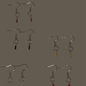 May include: Six pairs of handmade earrings with silver-colored hooks and beaded dangles in various colors, including red, black, gold, and silver. The earrings are displayed against a neutral background, showcasing their delicate design and craftsmanship.