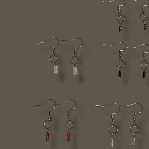 May include: A collection of handmade earrings with silver-tone hooks and circular accents. The earrings feature small, colorful beads in various shades, including white, red, black, and gold. The earrings are displayed against a neutral background.