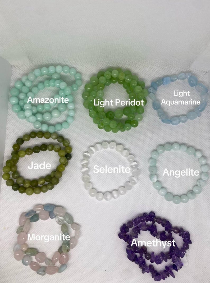 May include: An assortment of beaded bracelets in various colors and gemstones, including Amazonite, Light Peridot, Light Aquamarine, Jade, Selenite, Angelite, Morganite, and Amethyst. Each bracelet is displayed on a white surface.