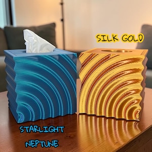 May include: Two decorative tissue box covers. One is blue with a wave pattern and the text "Starlight Neptune". The other is gold with a curved line design and the text "Silk Gold". Both are on a wooden table.
