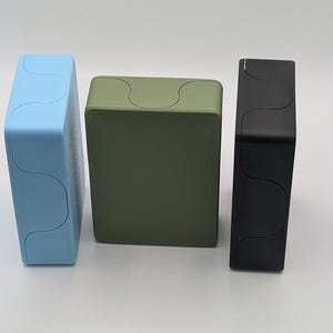 May include: Three rectangular boxes in a row, each with a unique color. The first box is light blue, the second is olive green, and the third is black. Each box has a wavy design on the top.