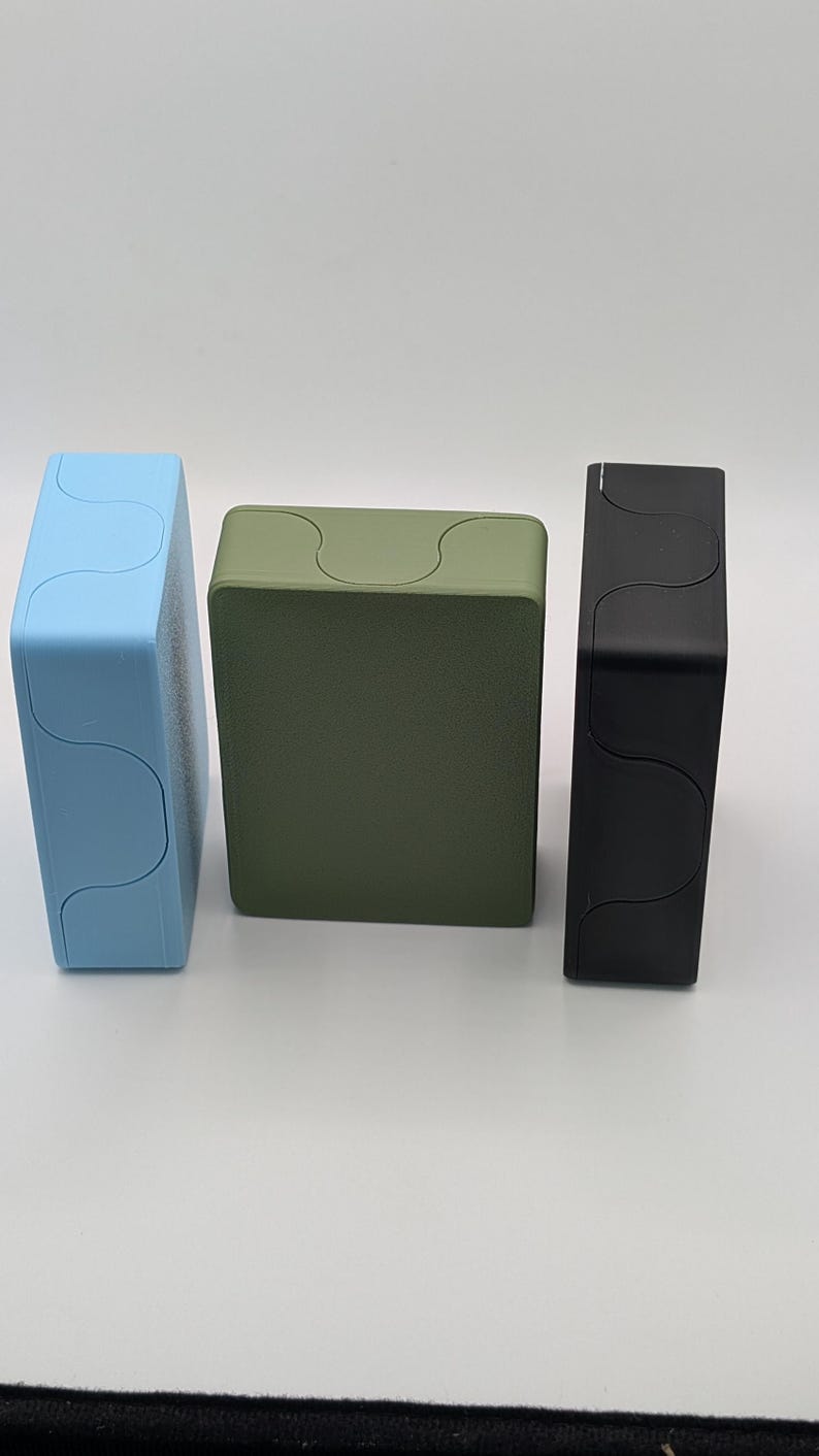 May include: Three rectangular boxes in a row, each with a unique color. The first box is light blue, the second is olive green, and the third is black. Each box has a wavy design on the top.