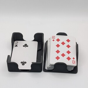 May include: Two black card holders with playing cards. One holder contains a two of clubs card, and the other contains a stack of cards showing the ten of diamonds. The cards are white with red and black symbols.