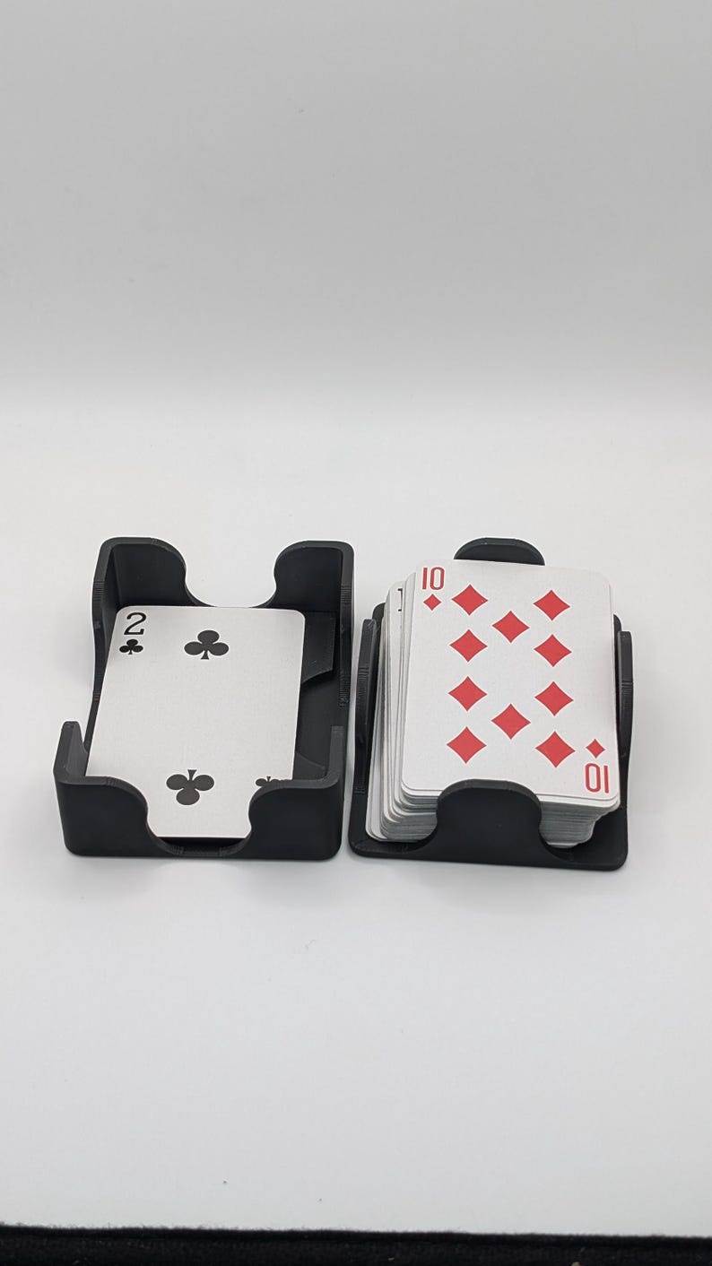 May include: Two black card holders with playing cards. One holder contains a two of clubs card, and the other contains a stack of cards showing the ten of diamonds. The cards are white with red and black symbols.
