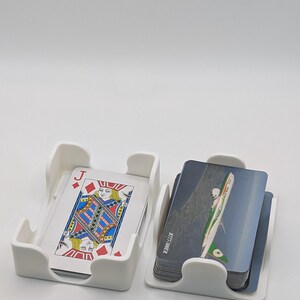 May include: Two white plastic card holders, each containing a stack of cards. One holder displays a playing card with a Jack of Diamonds design. The other holder contains cards with an image of an airplane. The text "B777-300ER" is visible on the side of the cards.