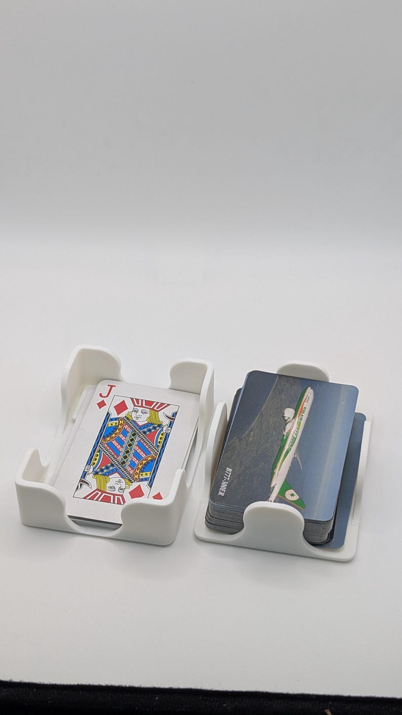 May include: Two white plastic card holders, each containing a stack of cards. One holder displays a playing card with a Jack of Diamonds design. The other holder contains cards with an image of an airplane. The text "B777-300ER" is visible on the side of the cards.