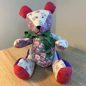 May include: A patchwork teddy bear with a floral print fabric. The bear has red ears, a green bow, and blue and white fabric on its legs.