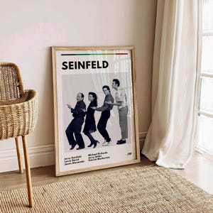 Könnte beinhalten: Ein Schwarzweiß-Poster mit einem Foto der vier Hauptdarsteller der Fernsehserie Seinfeld. Das Poster trägt den Titel "SEINFELD" in fetten schwarzen Buchstaben oben. Die Schauspieler sind Jerry Seinfeld, Michael Richards, Jason Alexander und Larry David. Das Poster enthält auch die Namen der Schauspieler und ihrer Charaktere. Das Poster ist in einem hellen Holzrahmen gerahmt.