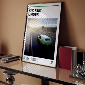 Puede incluir: Un póster con una imagen en blanco y negro de una carroza fúnebre verde conduciendo por un camino con una puesta de sol en el fondo. El texto "SIX FEET UNDER" está en la parte superior del póster. El póster también incluye los nombres de los actores y el año 2001.