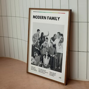 May include: A framed poster featuring the cast of "Modern Family." The poster has a white background with the show's title in bold black letters. The cast is in a black and white photo. The frame is a dark brown color.