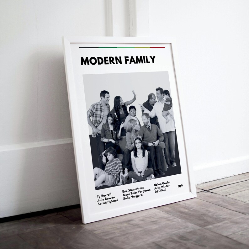 May include: A framed black and white poster featuring the cast of "Modern Family." The poster includes the show's title and the names of the actors. The image is set against a white background and leans against a wall.